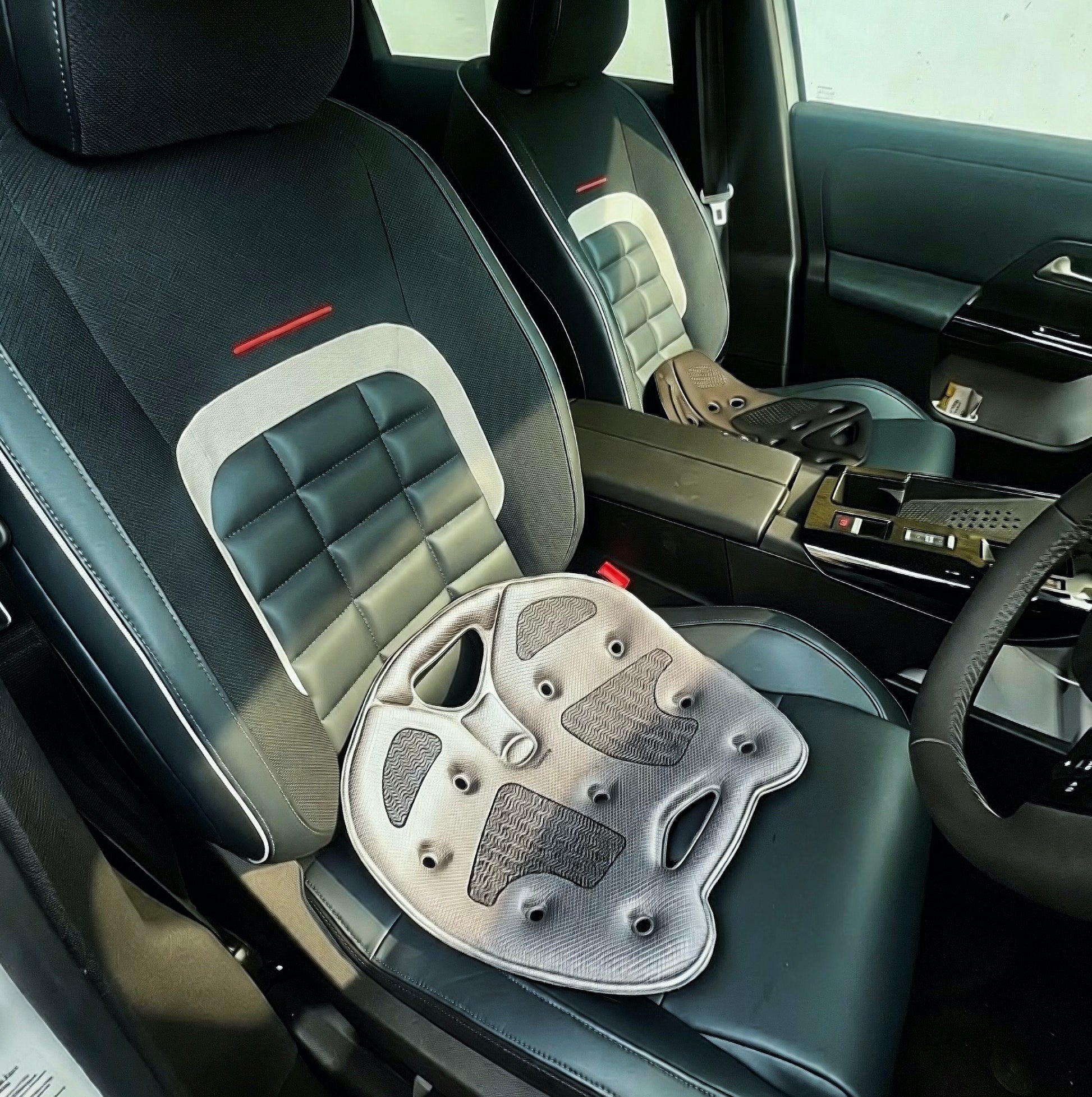 Gray BackJoy posture corrector seats resting on leather car seats to prevent driving fatigue and spine strain.